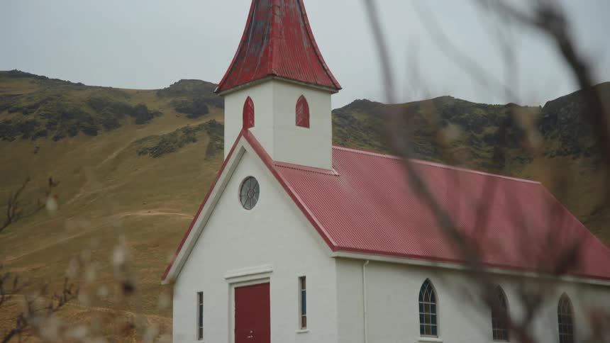 White church with red roof stands amid grass and hills with gravestones nearby