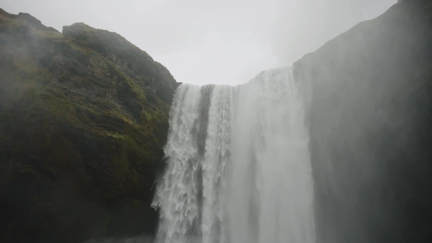 Looking up to massive waterfall flowing over a moss covered canyon in slow motion