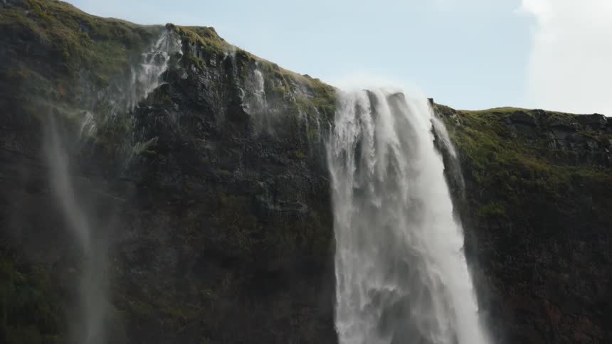 This is a video of a powerful waterfall cascading over a steep mosscovered cliff facethe water drops dramatically creating a wide curtain of white spray against the dark rugged cliff
