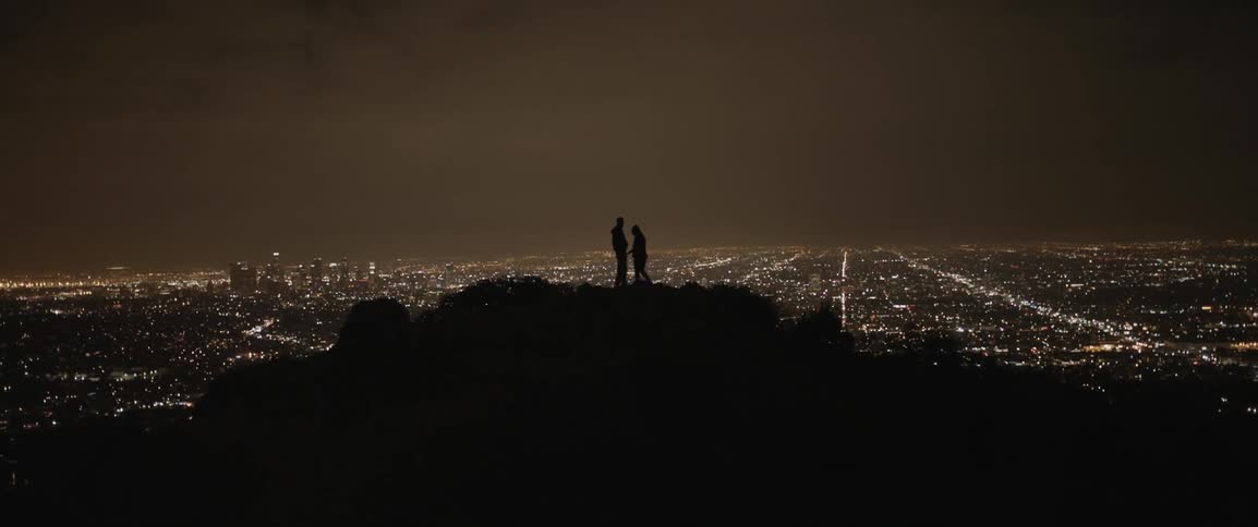 A man and woman hold hands on a hill overlooking city lights