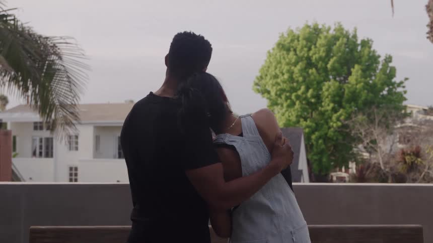 Young couple hugging while looking at a suburban neighborhood from a balcony outdoors during day time