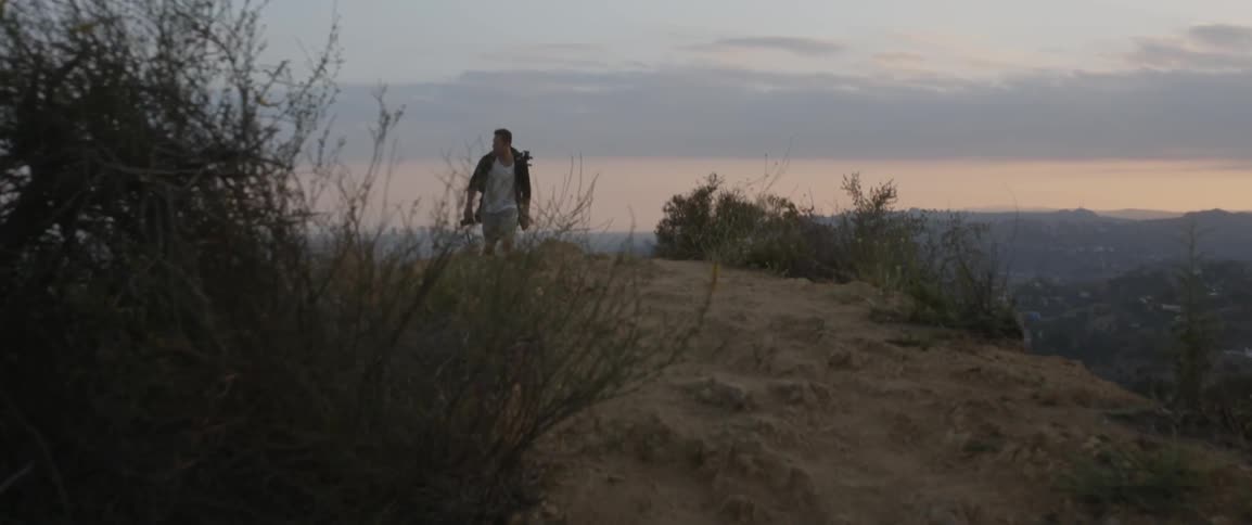 A man carrying a camera walks up a hill