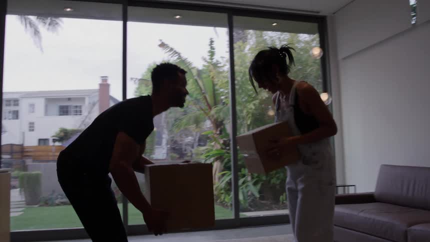 Two people lifting cardboard boxes in front of glass doors with garden in the background