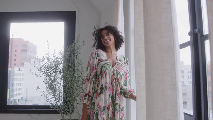 Woman smiles near the window while wearing a floral dress