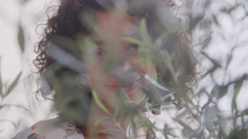 Woman smiles while partially hidden behind leaves