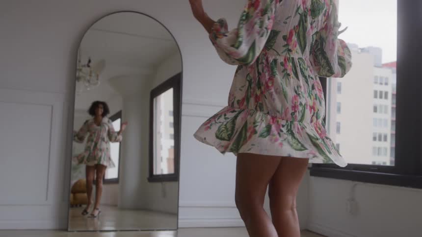 Woman tries on a floral dress while looking at herself in the mirror