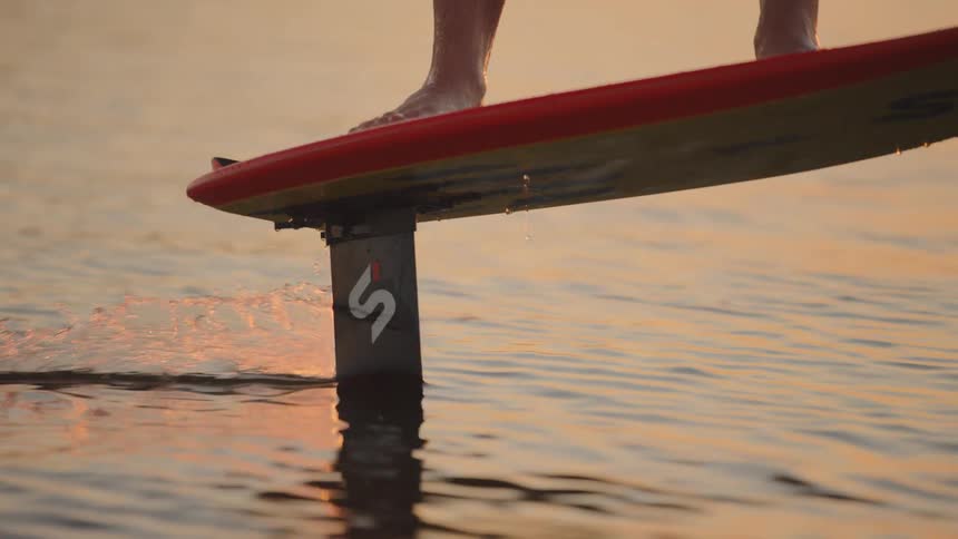 Person standing on hydrofoil board gliding over calm water at sunset