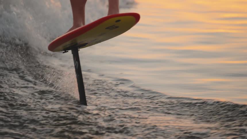 Man rides and electric surfboard above the water along the coast as waves roll in to shore