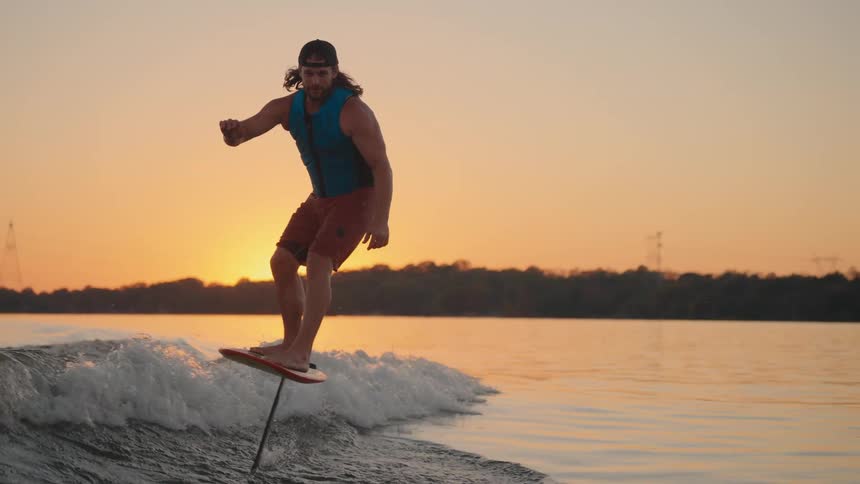 Person surfs with hydrofoil board over calm waters at sunset
