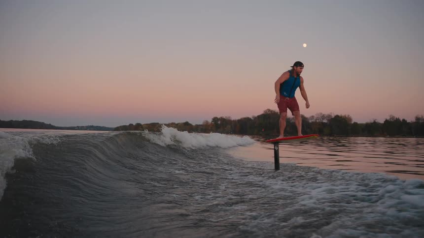 A man is wake foiling across a lake at sunset