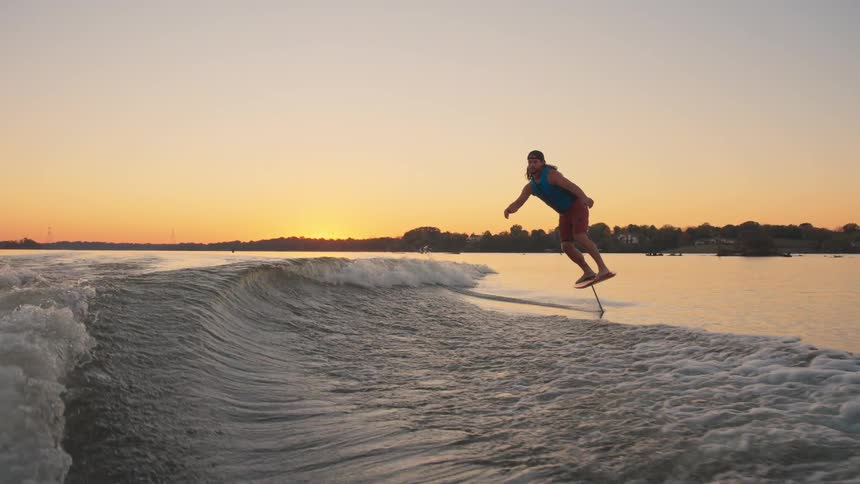 Person balancing hydrofoil board over rippling water at sunset with vegetation in the background