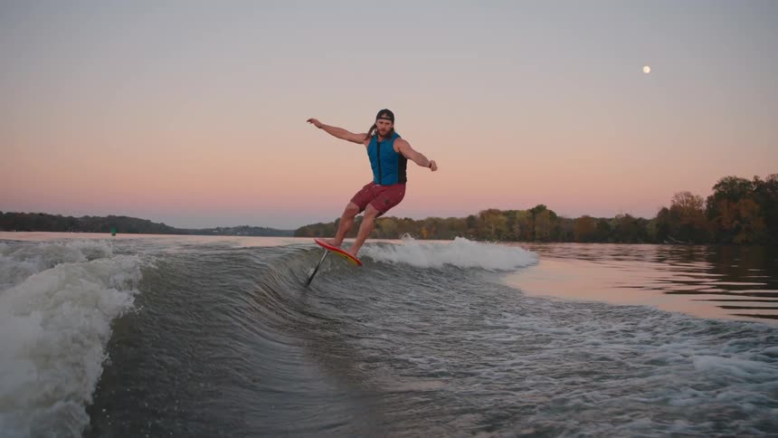 Man surfs on a foil board while gliding along the wave at sunset