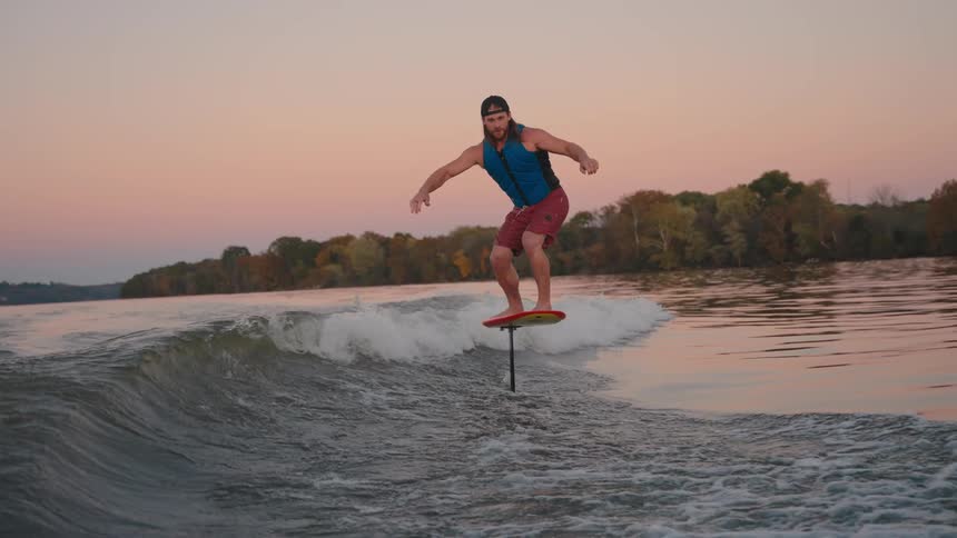 A man foil surfs on a boats wake during a beautiful sunset over a wide lake