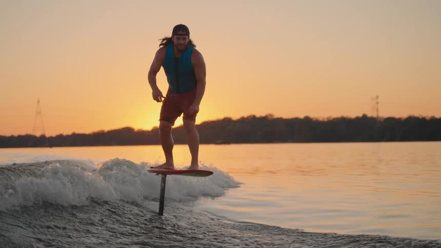 Person rides hydrofoil board over calm waters at sunset surrounded by tranquil nature