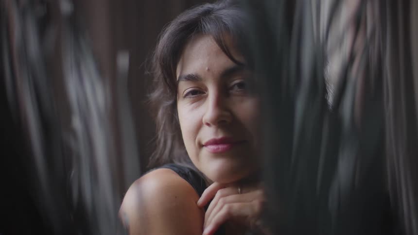 A womans face is shown in a closeup shot looking past vertical foreground material and she changes her expression from a serious gaze to a slight smile