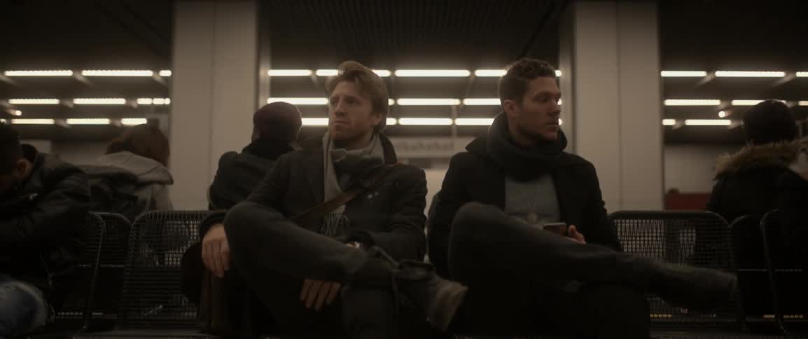 Two men sit at a bus station waiting