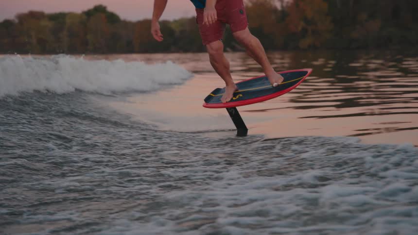 Man surfs on a foil board balancing over the water at sunset