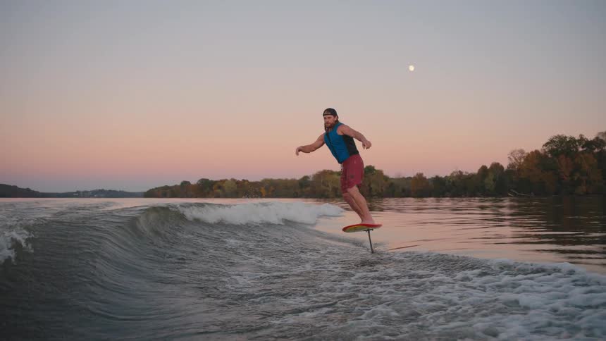 A man rides a hydrofoil surfboard on a lake at sunset