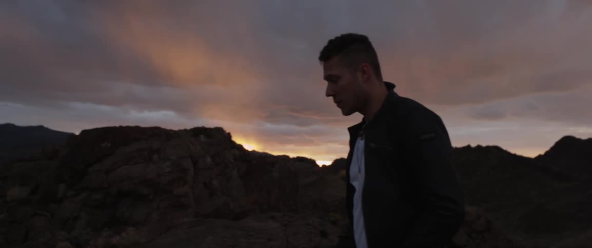 A man is walking on a mountain looking towards the sunset