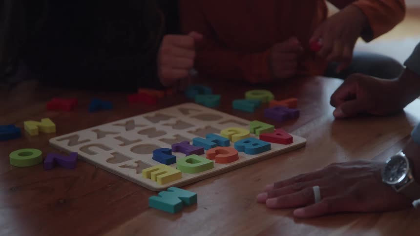 Child interacting with colorful letter board alongside adults on wooden floor