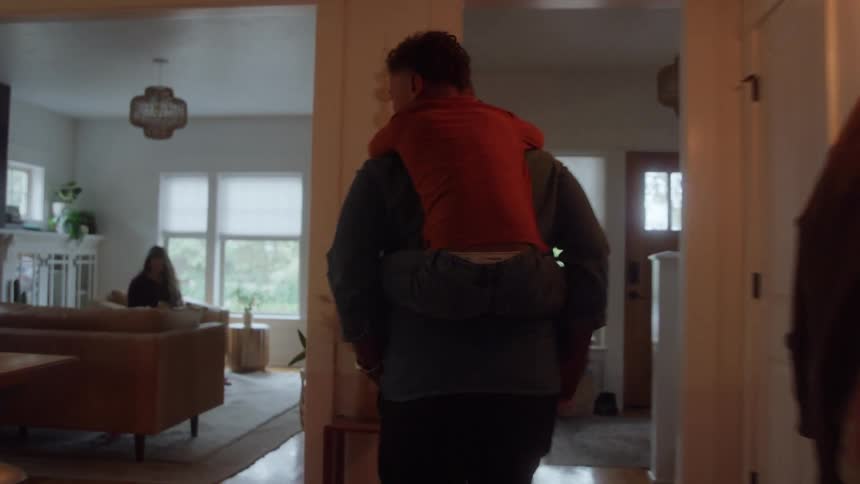 Man walks carrying a child on his back inside the house