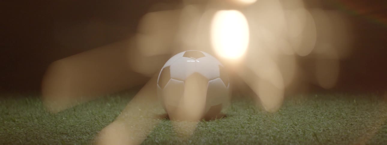 Soccer ball rests on grass lit by warm lights in cinematic scene