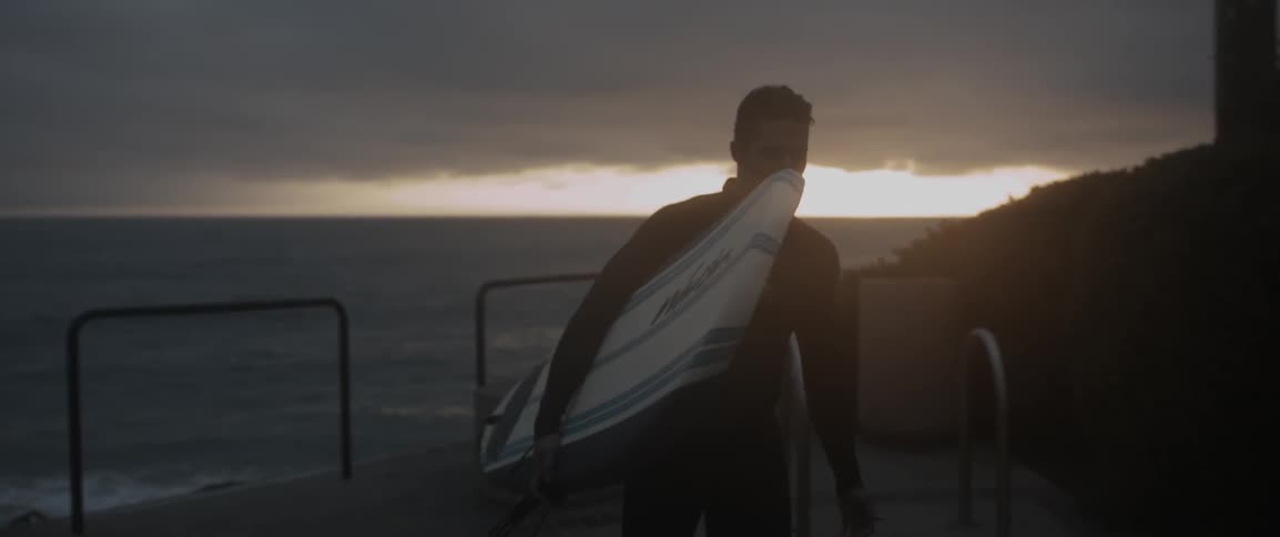A surfer carries a surfboard at sunset