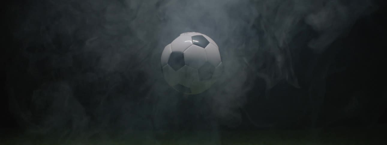 This video features a soccer ball suspended in midair against a dark background completely enveloped by swirling thick smoke or fogthe ball is brightly lit contrasting with the dark moody atmosphere as the smoke slowly dissipates revealing the b