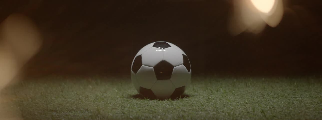 Black and white soccer ball on lit grass with dark background