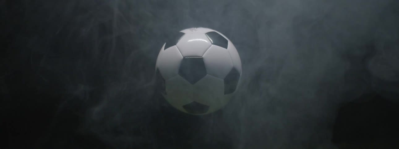 Black and white soccer ball floating amid mist against dark background