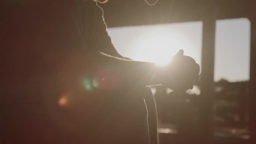 A silhouette of a man with his hands clasped is framed by a bright sunburst from a window creating a dramatic halo effect