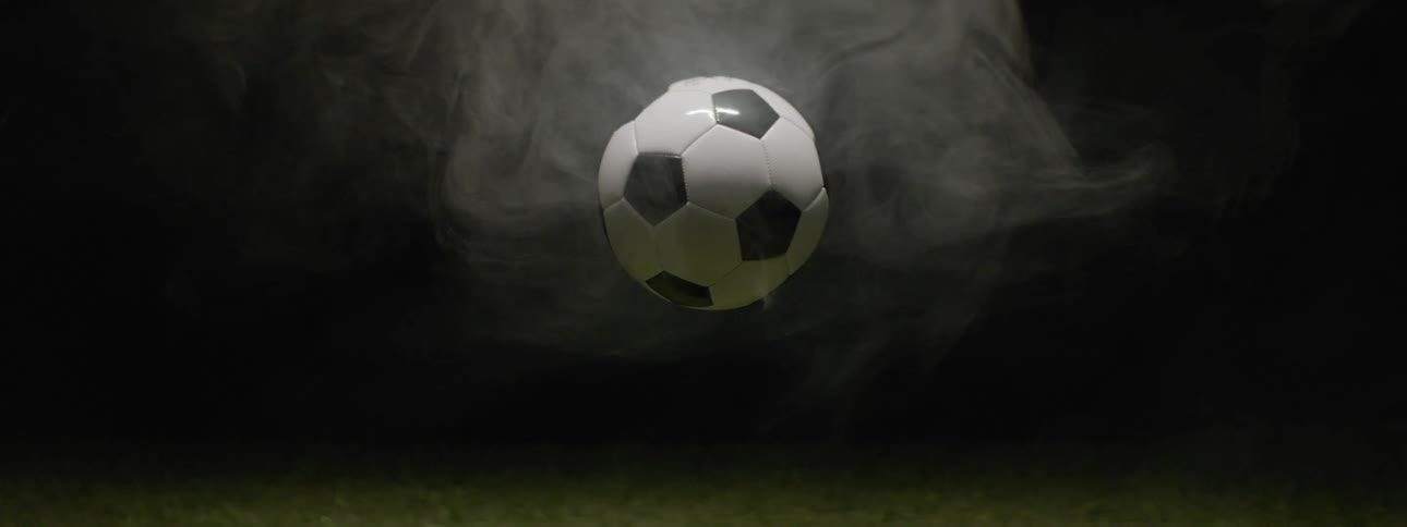 Soccer ball hovers above dark grass surrounded by mist in dramatic background