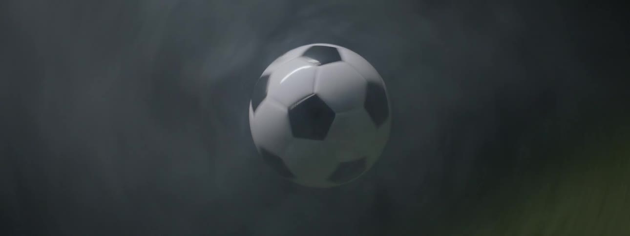A blackandwhite soccer ball is suspended and slowly rotating in the center of the frame surrounded by wispy gray smoke that obscures the background
