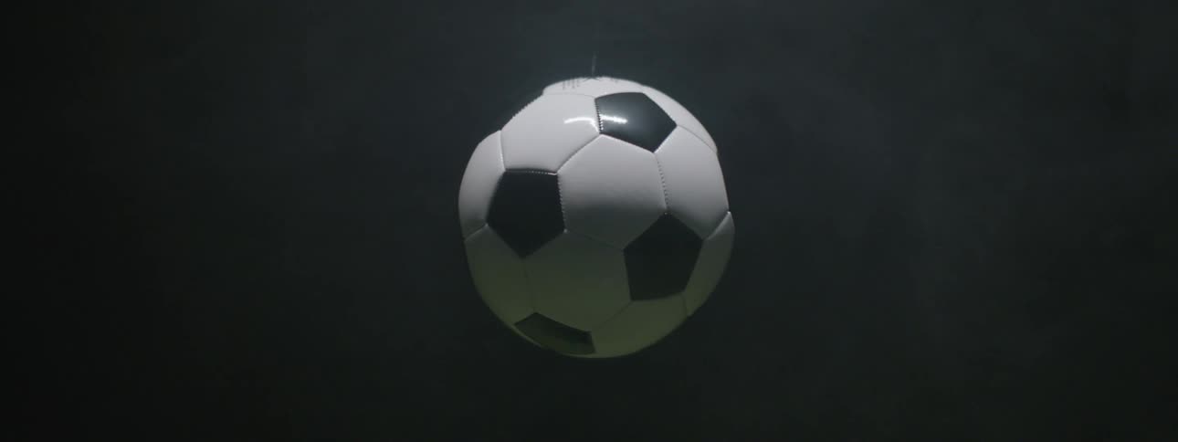 This short video shows a traditional black and white soccer ball football hanging suspended against a dark featureless background it appears to be swaying very gently almost imperceptibly on a thin string or wire