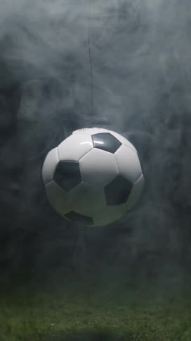 The video centers on a classic blackandwhite soccer ball suspended in midair against a dark background of what appears to be a grass fieldthe ball is initially obscured by a veil of white smoke or fog that slowly dissipates revealing the ball and
