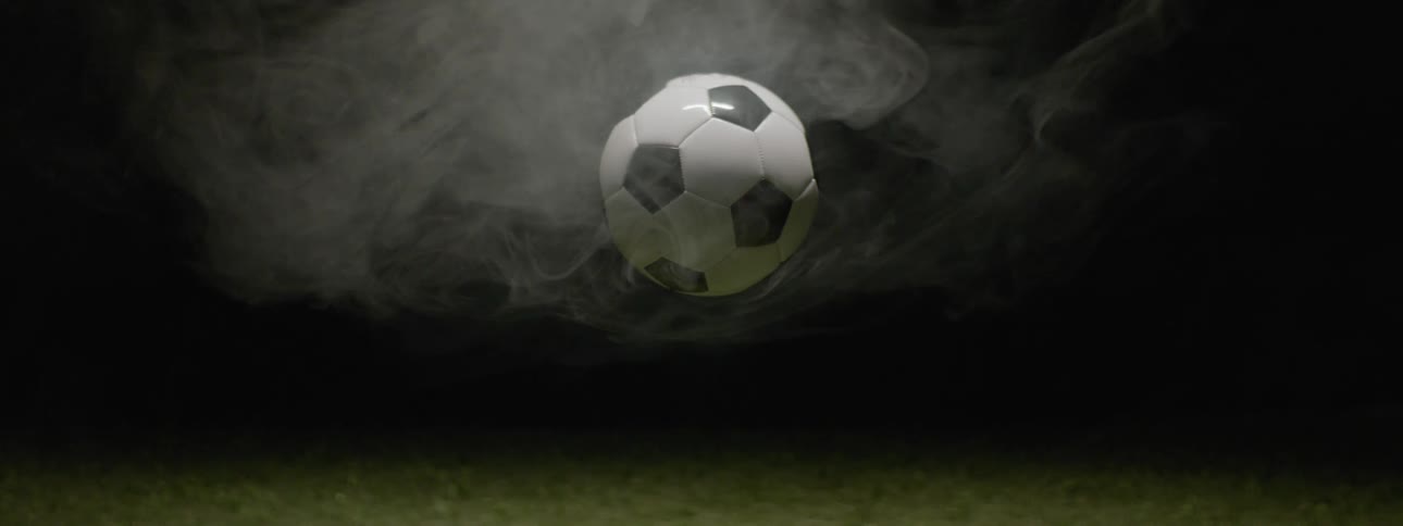 A soccer ball rests motionless in an open area at night surrounded by drifting white smoke