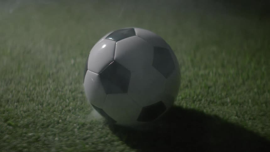 This video shows a classic black and white soccer ball spinning rapidly and then settling down on a patch of green grass the dynamic camera angle emphasizes the motion and the impact of the ball coming to rest