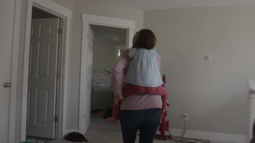 Mother carrying her daughter while walking into a room of the house