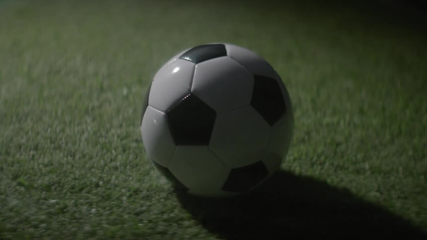 The camera violently spirals toward a stationary soccer ball on dark turf creating a chaotic green vortex of motion blur that snaps abruptly into a sharp static closeup
