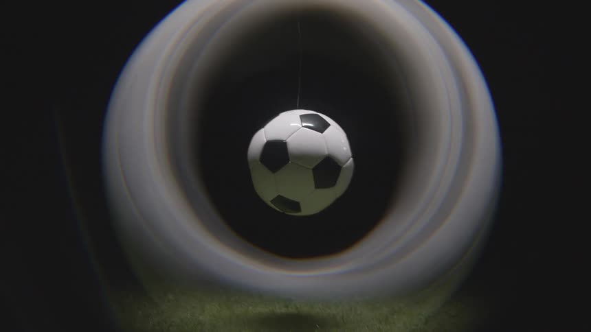 Soccer ball hanging by thin string over grass with dark background and circular visual effect