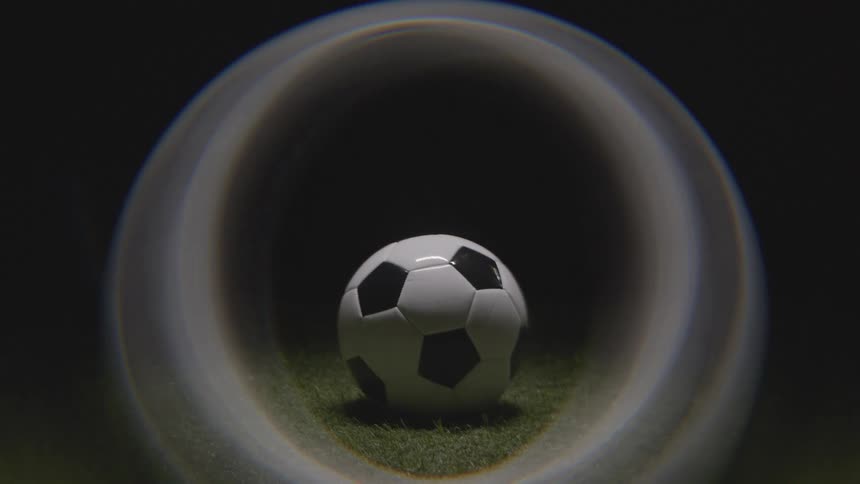 A black and white panel soccer ball resting on green grass turf with the ball slowly coming into sharp focus within the center of the illuminated circular area