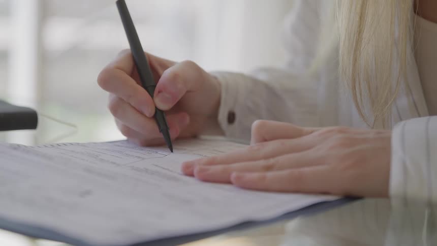 Closeup of hands signing a document with a black pen on a reflective desk in an office