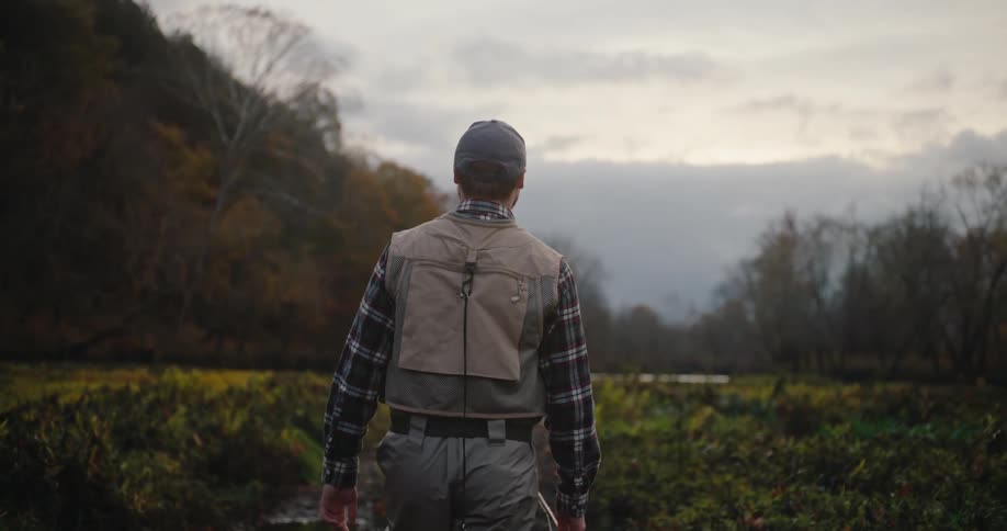 Man walks through a wet field wearing fishing gear at dusk