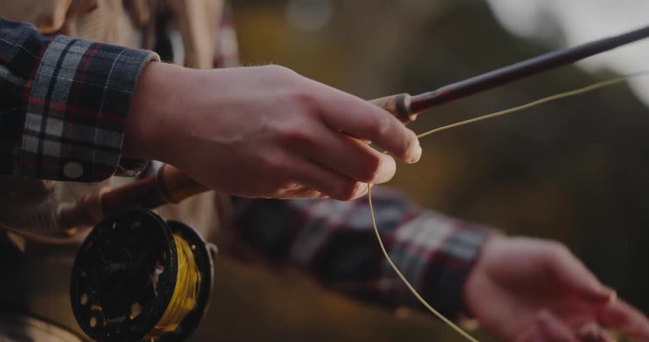 Hands adjusting fishing line with reel in focus over plaid shirt