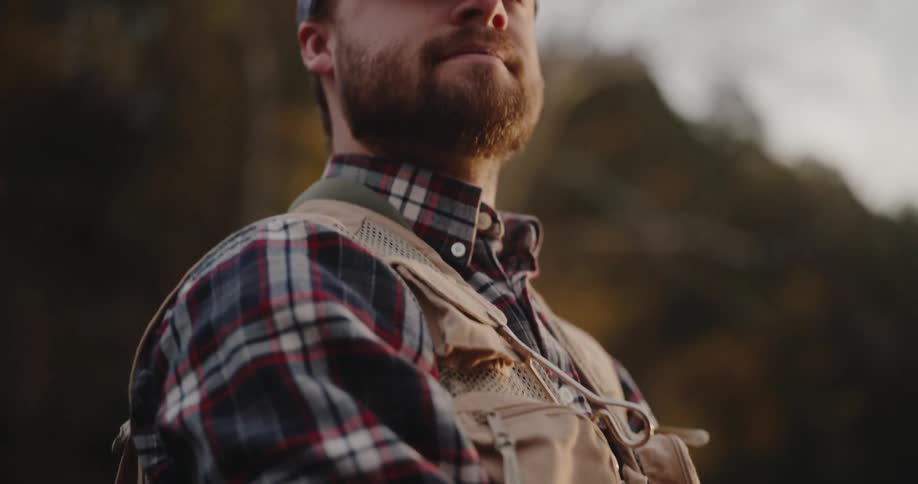 Person in plaid shirt and waders holding fly fishing rod with line in motion at sunset