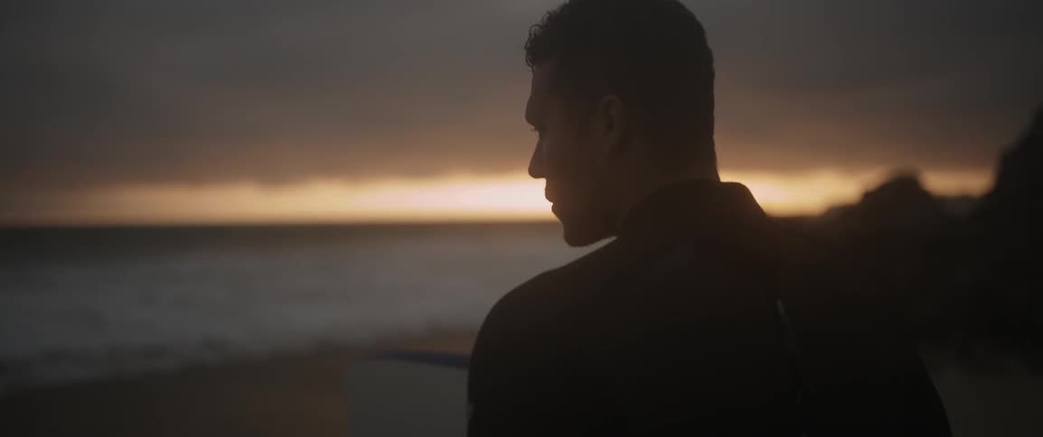 A man in a wetsuit looks out toward the ocean at sunset