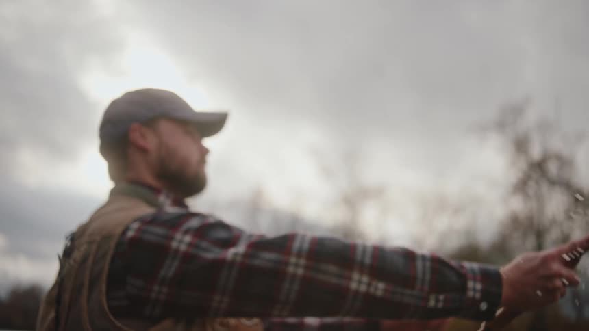 Man in plaid shirt and cap casting fly fishing line under cloudy sky