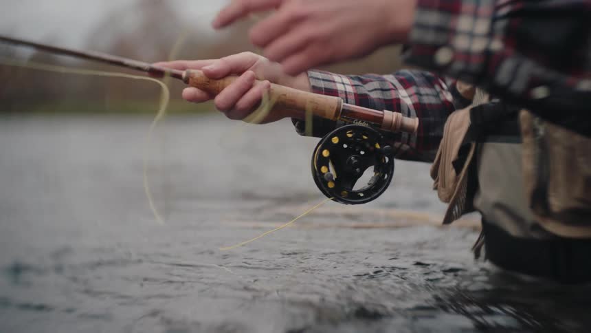 Male hands rolling the string on a fishing rod outdoors during day time