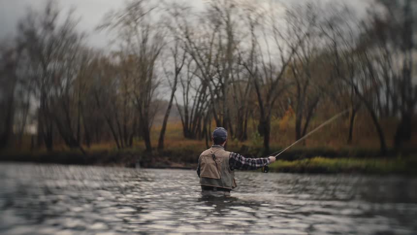 Person fly fishes in calm river during autumn