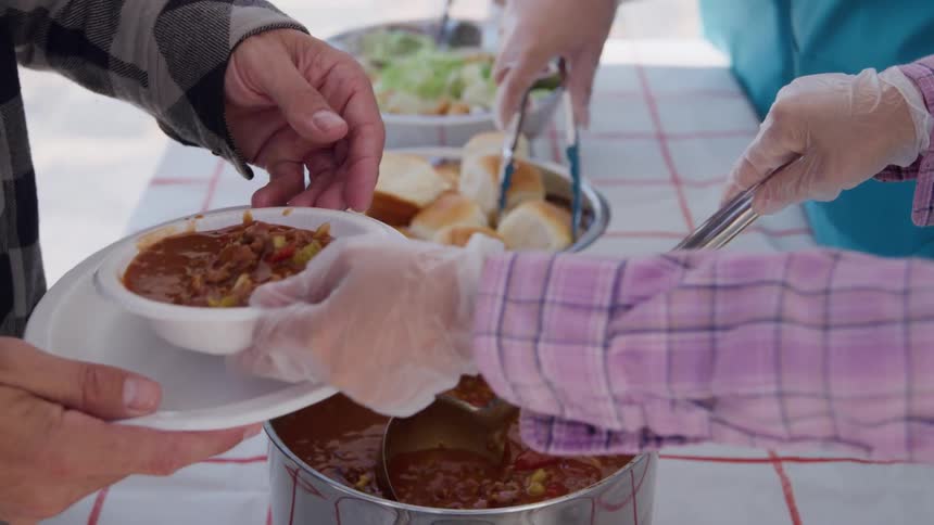 Food distribution service filling a plate with hot soup